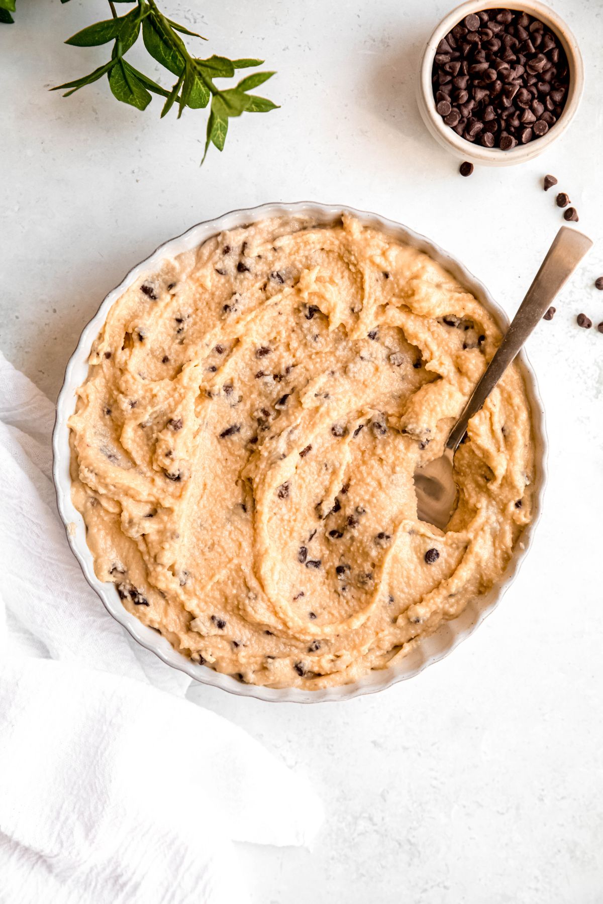 overhead shot of a white table with a white serving bowl filled with cottage cheese cookie dough with mini chocolate chips scattered around.