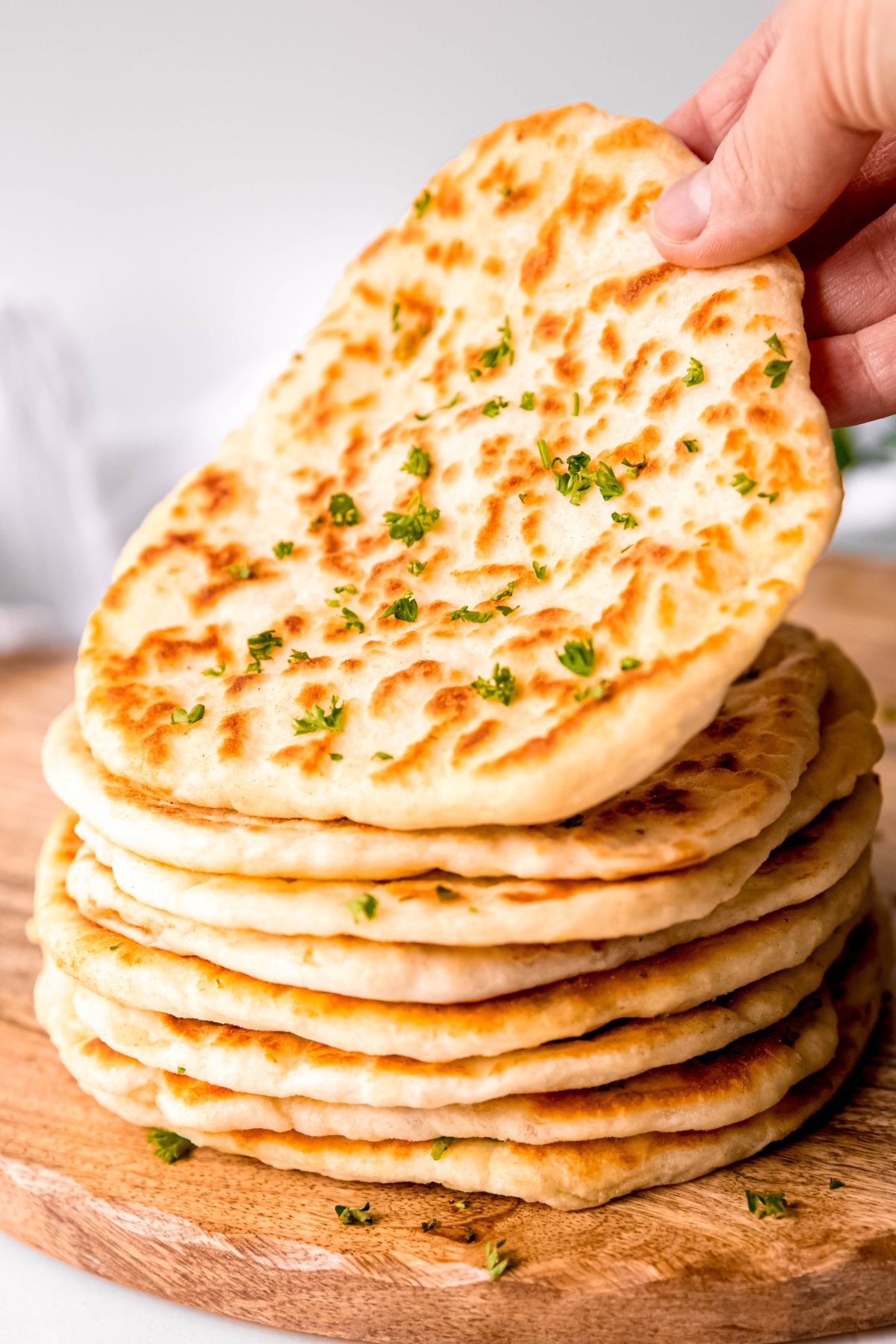 hand lifting up the top piece of cottage cheese flatbread from a stack on a wooden surface.