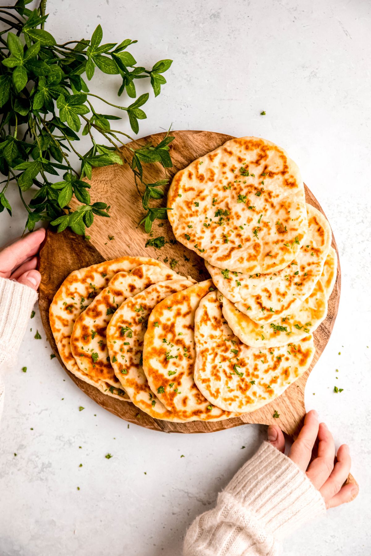 hand setting down a wooden pizza peel with homemade high protein cottage cheese flatbreads spread out in a semicircle on a white table.