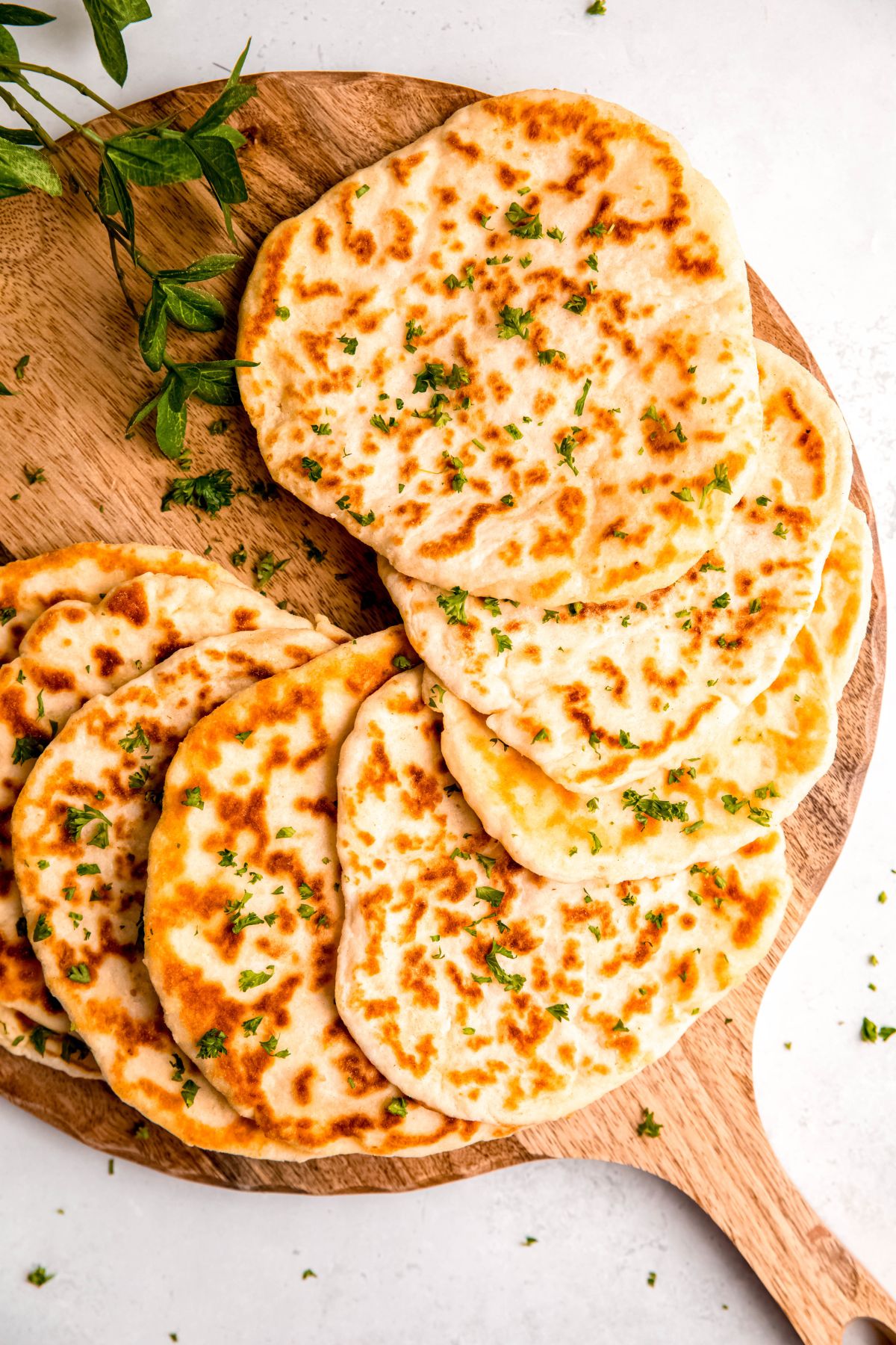 wooden pizza peel with 8 homemade cottage cheese flatbreads sprinkled with fresh parsley.