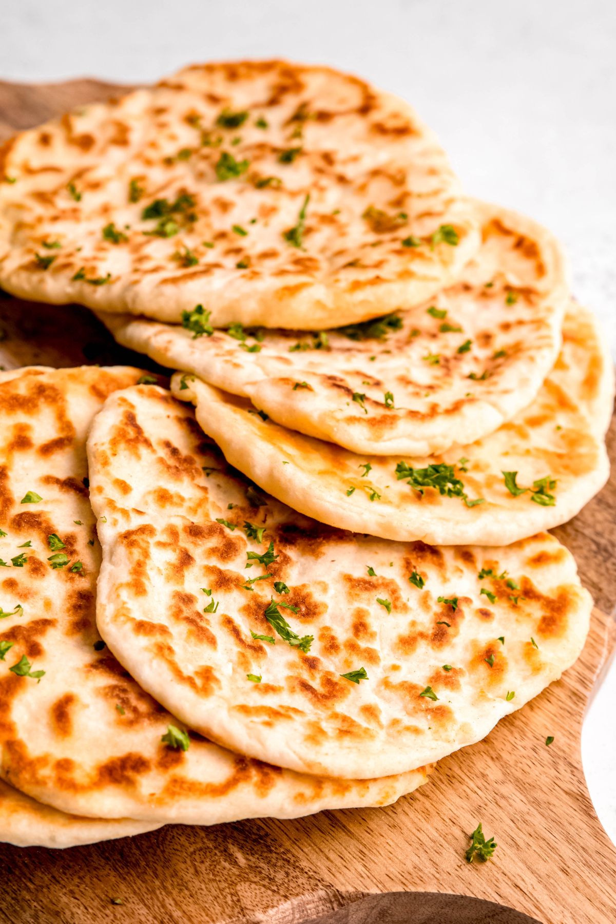 closeup shot of an array of cottage cheese flatbread pieces on a wooden surface topped with a sprinkle of parsley.