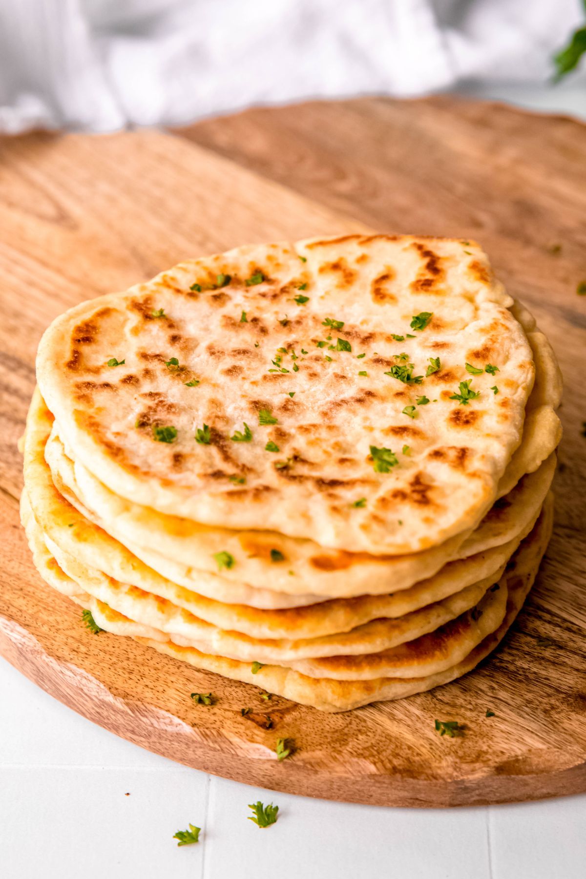 45 degree angle shot of a stack of homemade cottage cheese flatbreads on a wooden pizza peel on a white table.