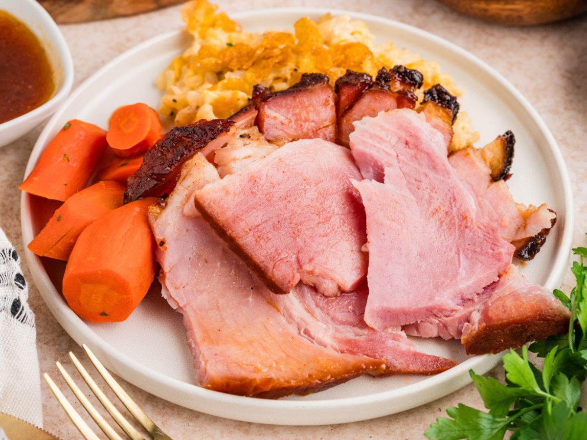 horizontally framed closeup shot of a plated portion of glazed double smoked easter ham with glazed honey roasted carrots and corn casserole.