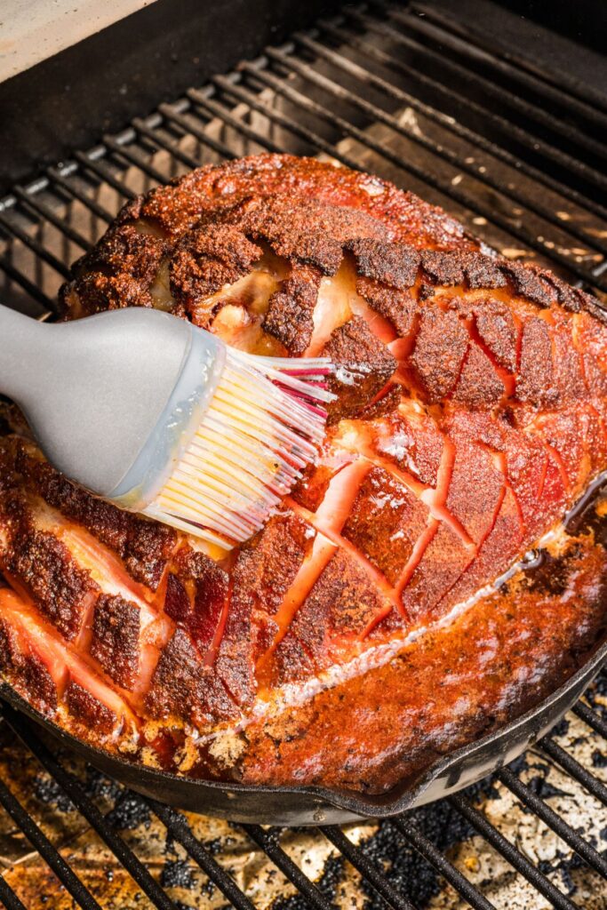 pastry brush brushing the glaze on the mostly-cooked ham in the smoker.