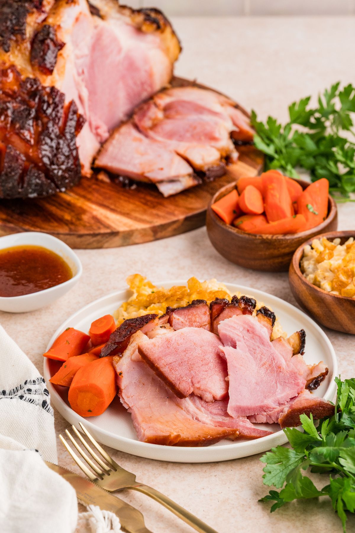 dinner plate with slices of double smoked glazed Easter ham with honey glazed carrots and corn casserole with more ham and sides in the background.