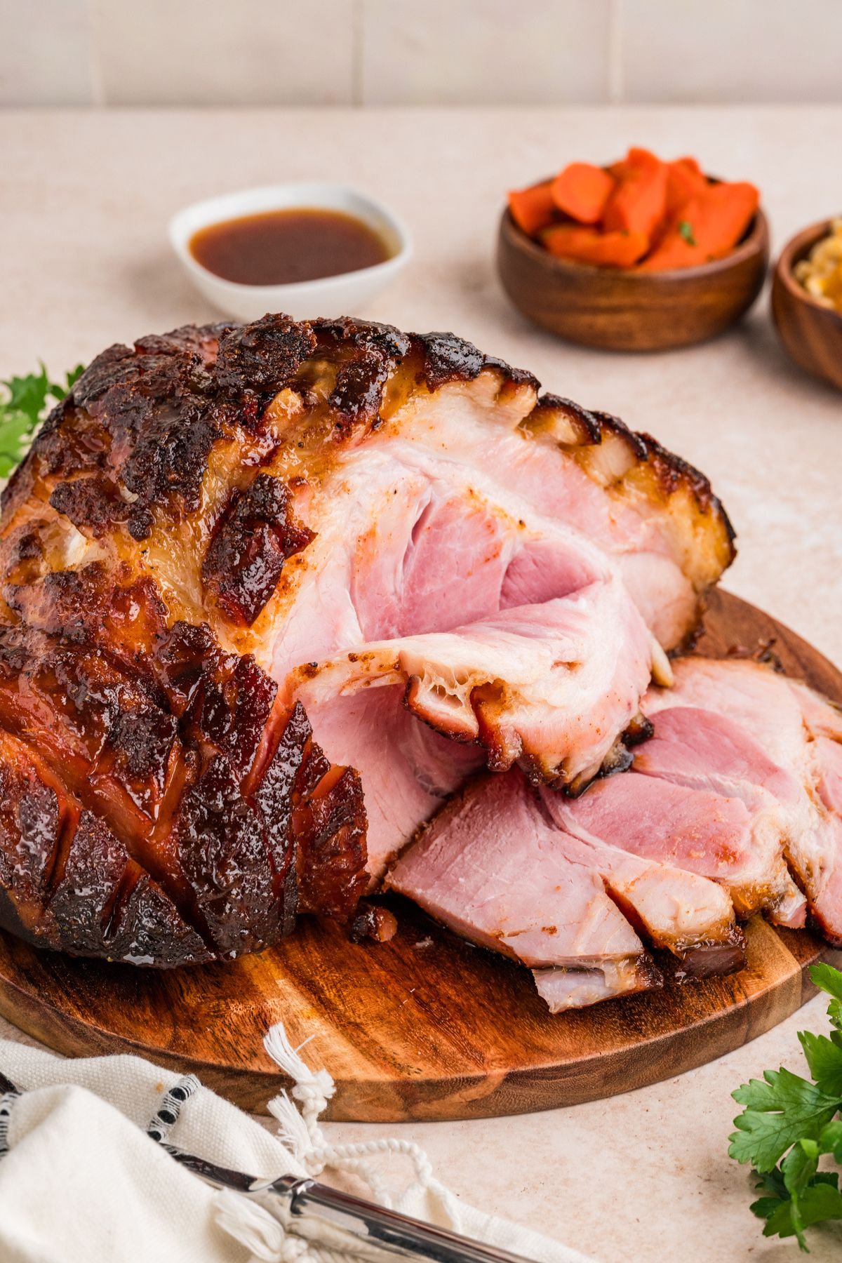 double smoked ham with honey apple glaze on a wooden cutting board with a few slices made to expose the pink meat inside as a foil to the crispy, glistening dark golden exterior.