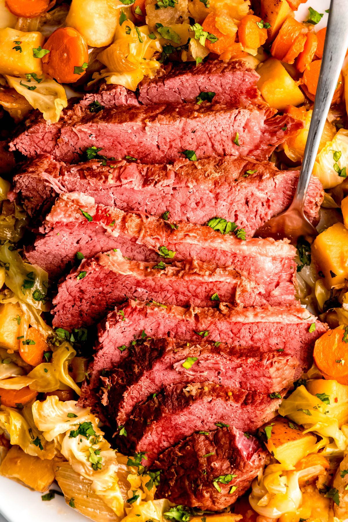 An overhead shot of sliced Dutch oven corned beef on cabbage, carrots, and potatoes.