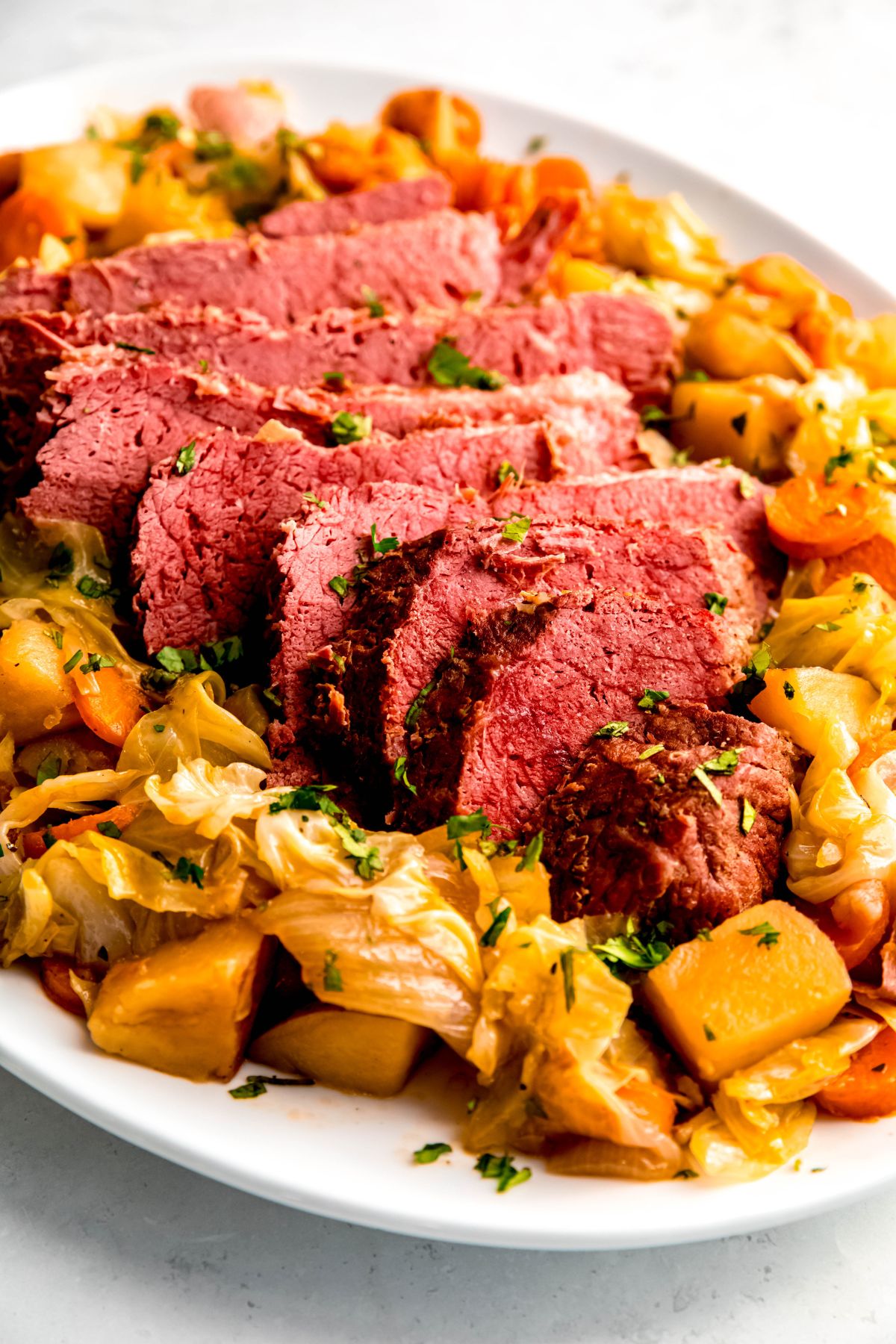 A close up shot of Dutch oven corned beef sliced and served on a platter of cabbage, potatoes, and carrots.