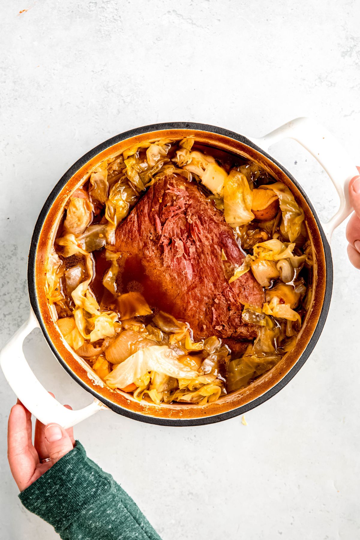 Two hands serving a pot of Dutch oven corned beef.
