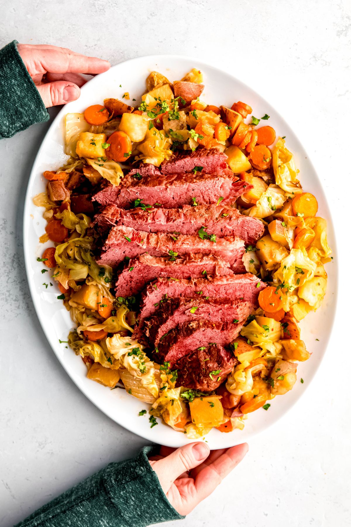 Two hands serving a platter of Dutch oven corned beef.