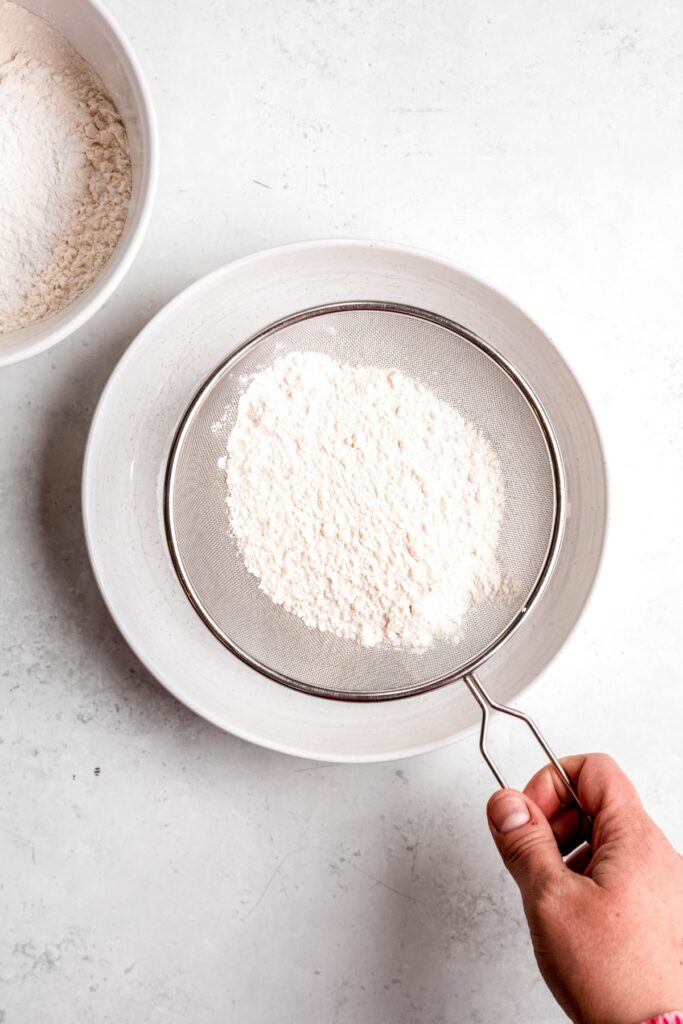 hand using a mesh sifter to make self-rising flour with all-purpose flour.