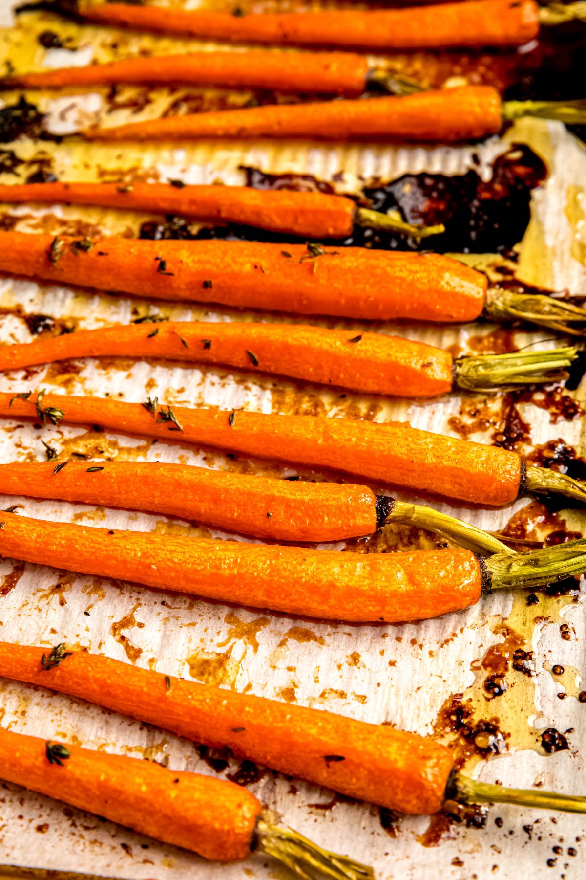 closeup shot of roasted brown sugar honey glazed carrots on a baking sheet after roasting and garnishing with extra thyme.