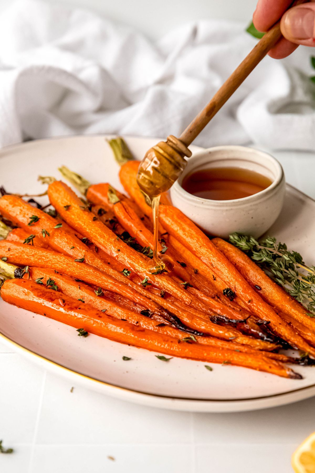 action shot of a wooden honey dipper drizzling extra brown sugar honey glaze onto the roasted carrots.