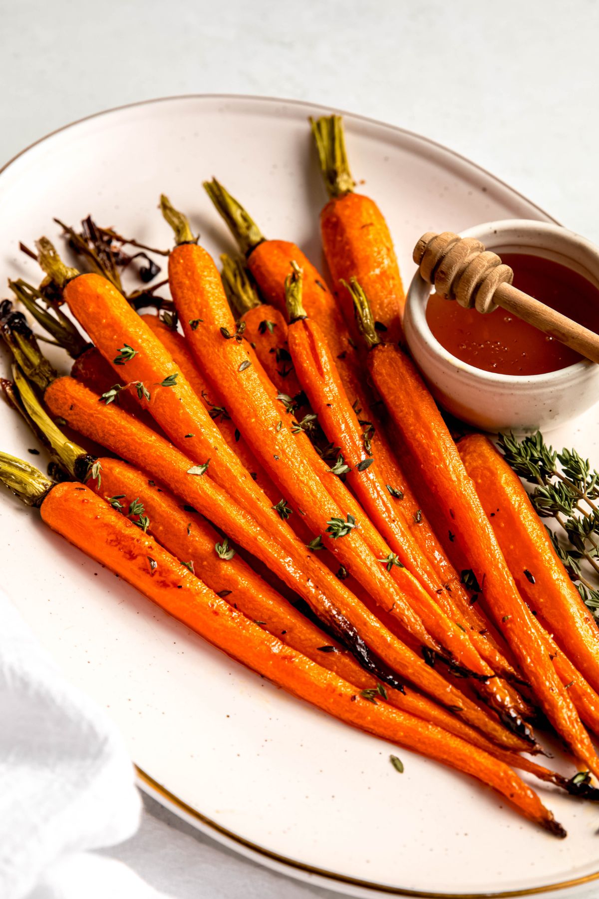 closeup shot of a platter of brown sugar honey glazed carrots on a white plate with a small bowl of extra glaze and a wooden honey dipper.