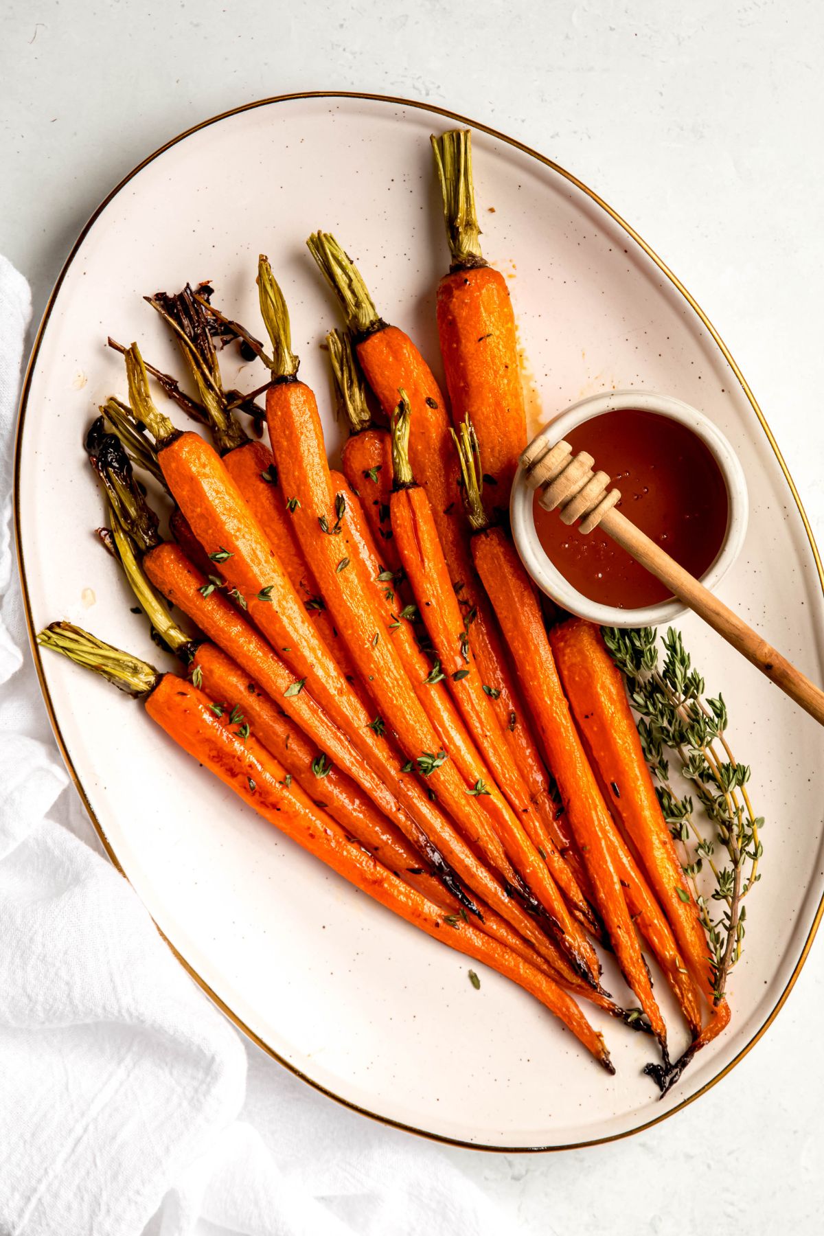 overhead shot of a serving platter of glazed carrots with brown sugar and honey glaze with an extra sprig of thyme and a ramekin of extra glaze with a honey dipper on the side.