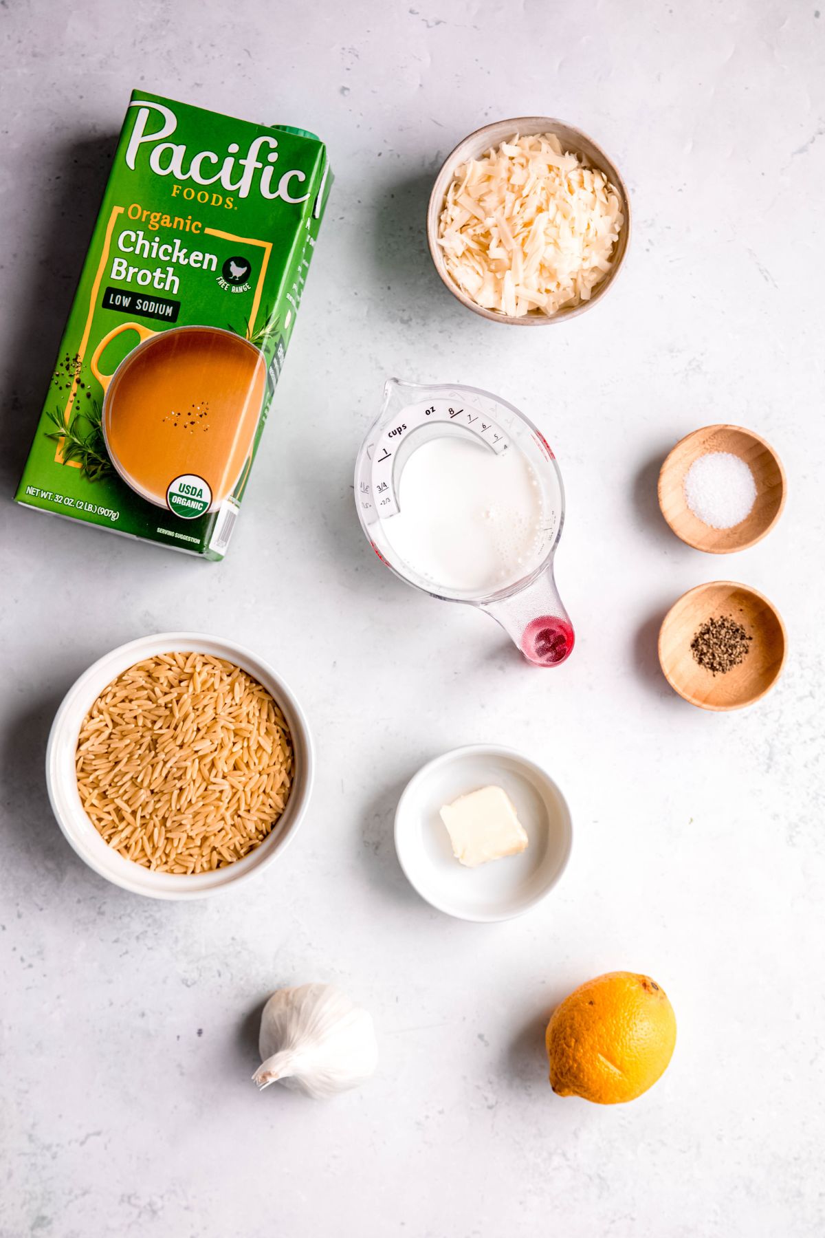 ingredients needed to make one-pot lemon orzo pasta recipe measured out on a white table.