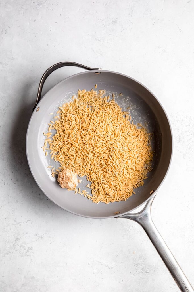 dry orzo pasta in a deep-sided skillet with a knob of butter for toasting.
