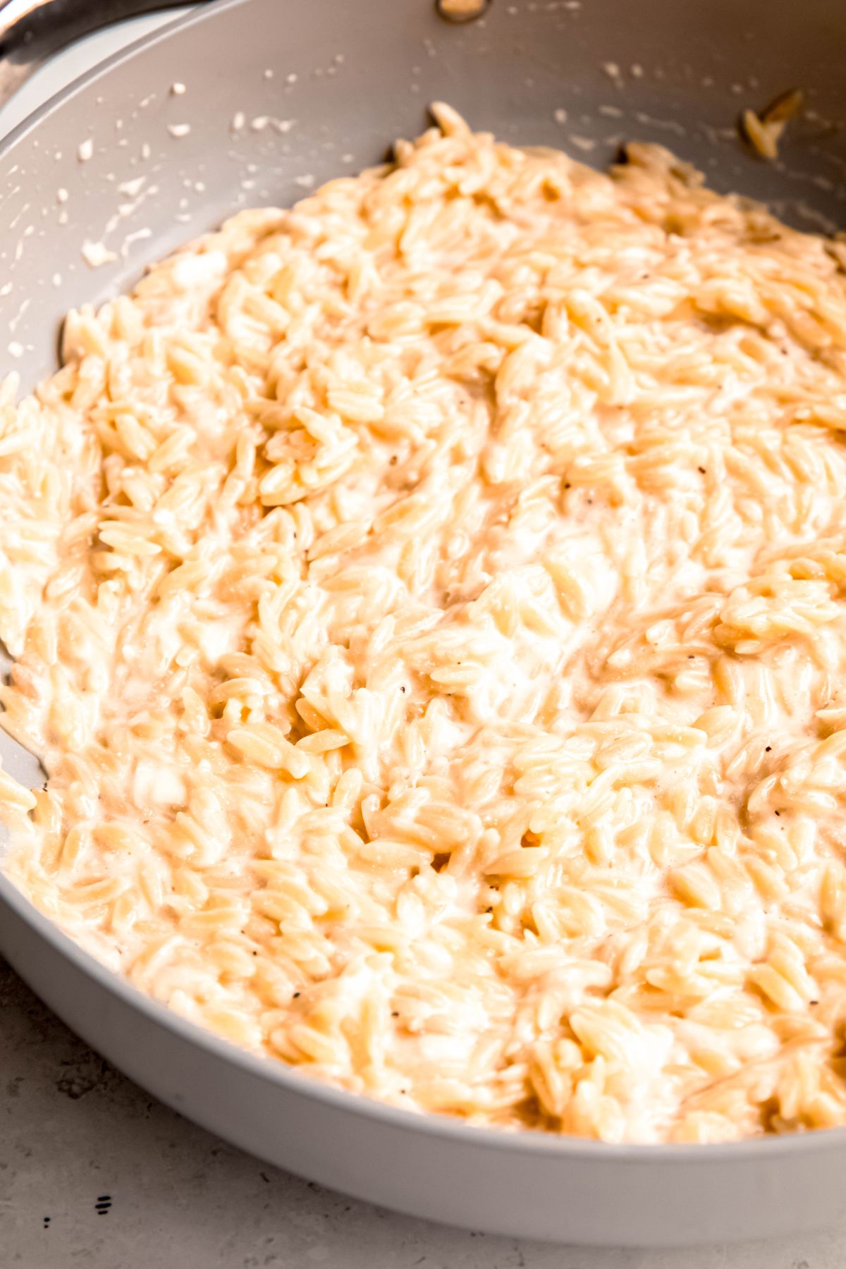 closeup shot of creamy lemony orzo pasta in the skillet after stirring in the cream and parmesan; you can see the risotto-like texture.