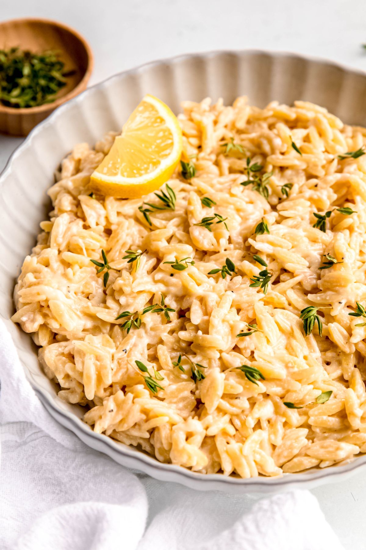 closeup 45 degree angle overhead shot of a serving bowl filled with lemon parmesan orzo pasta on a white table with a white cloth.