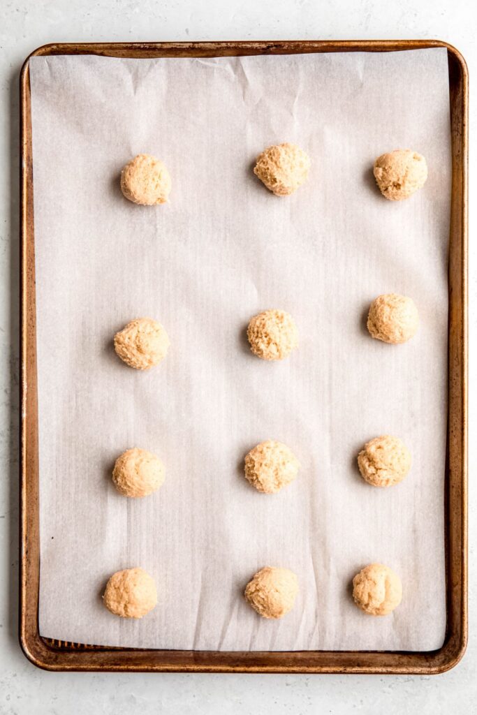 12 balls of lemon ricotta cookie dough on a parchment lined baking sheet.