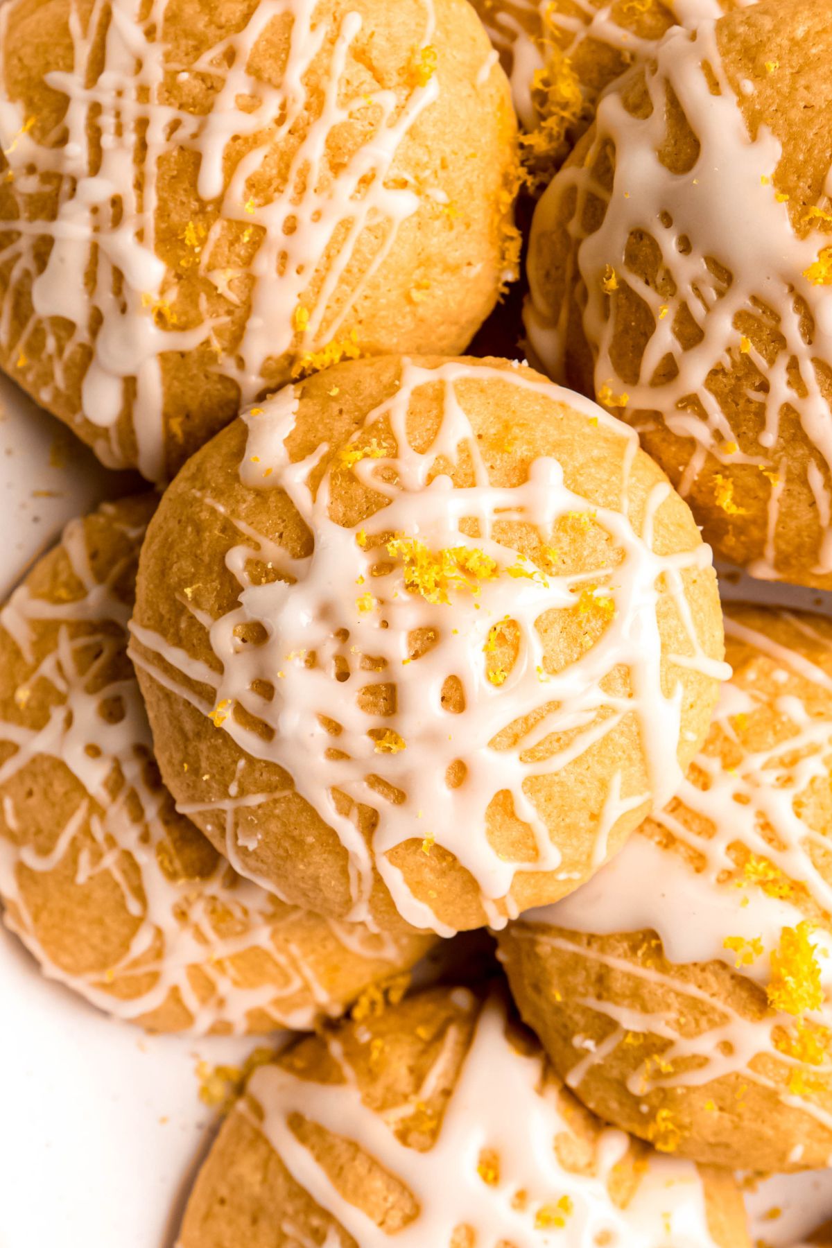 closeup overhead shot of a pile of whole wheat lemon ricotta cookies with a lemon glaze and extra lemon zest.