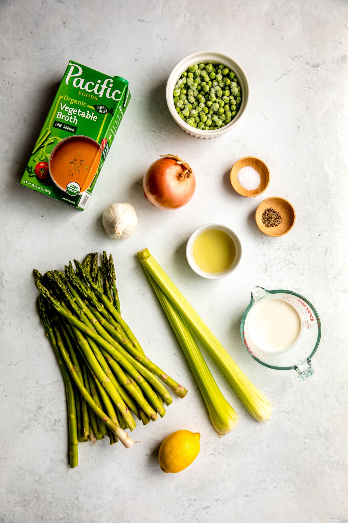 ingredients needed to make cream of asparagus soup recipe measured out on a white table.