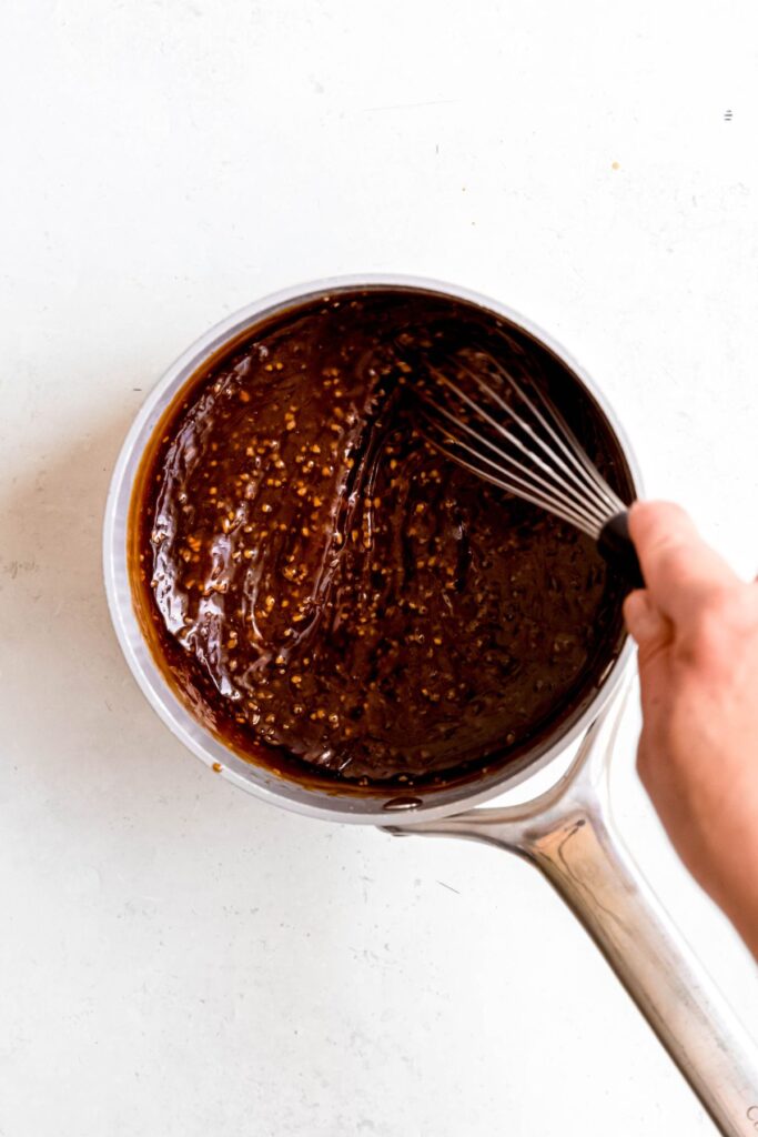 action shot of a hand whisking teriyaki sauce in a saucepan after adding the cornstarch for thickening; you can see the viscous consistency.