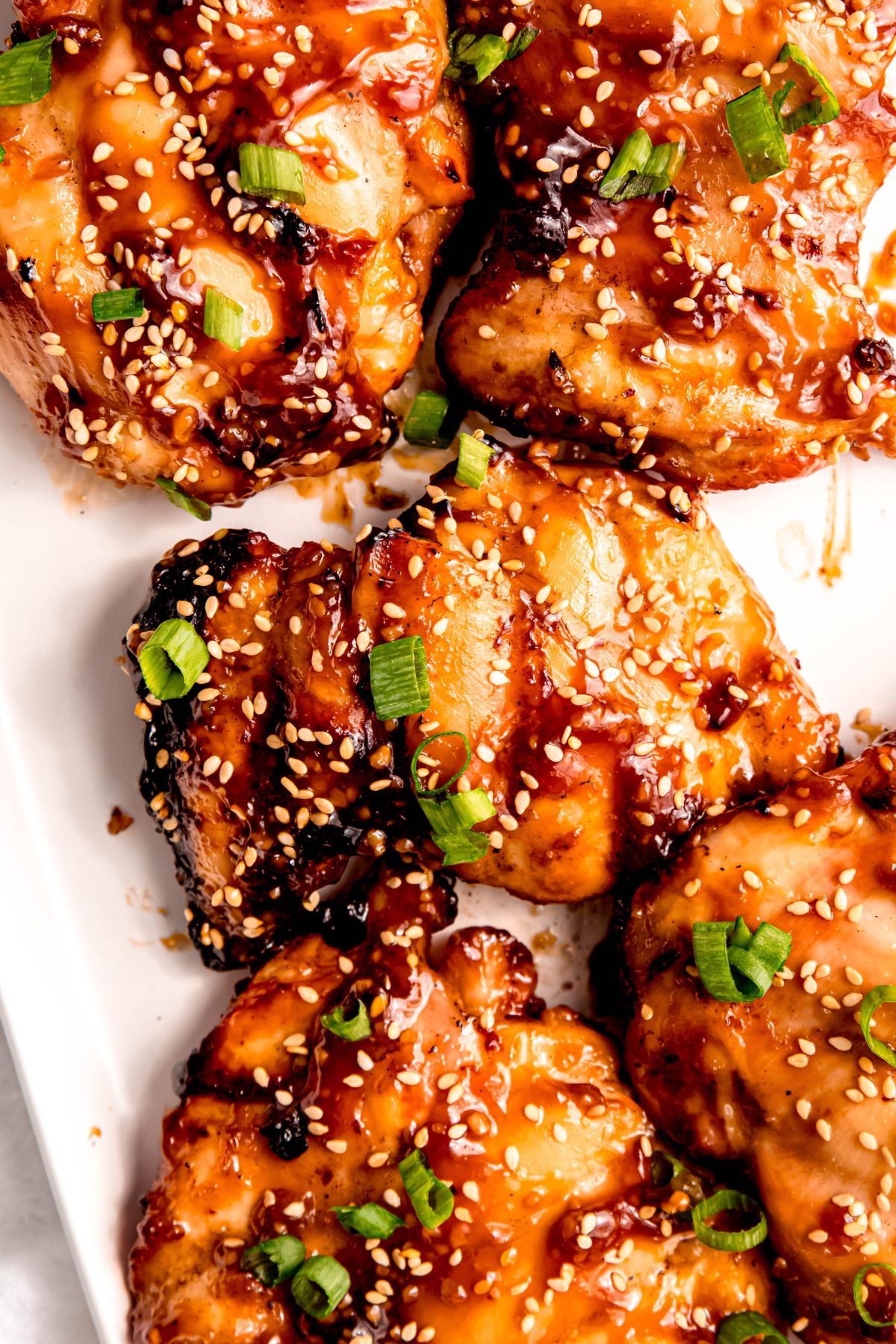 closeup overhead shot of charbroiled teriyaki chicken from the grill on a white serving platter.