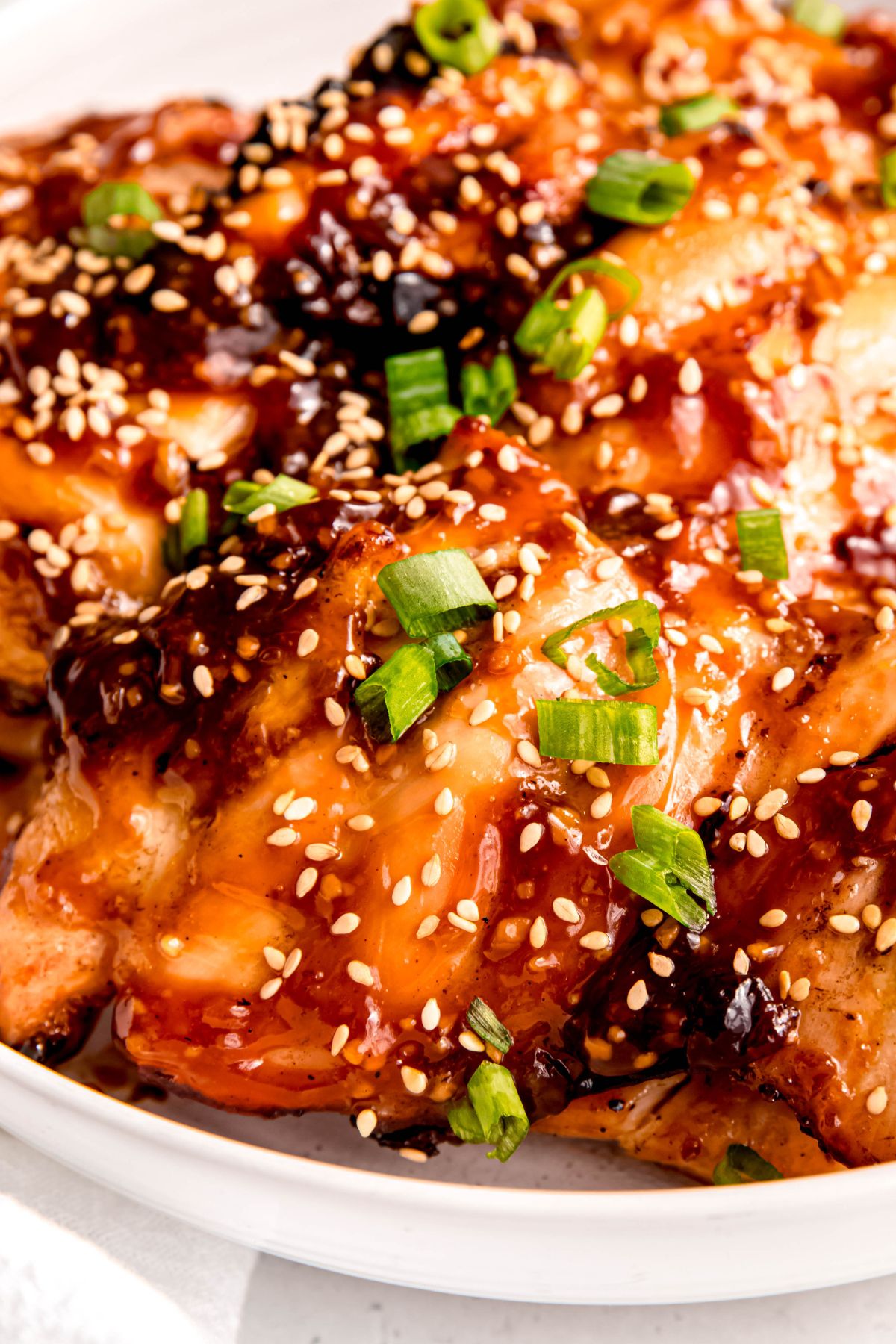 closeup shot of grilled teriyaki chicken on a white plate with toasted sesame seeds and scallion greens clinging to the sticky-sweet sauce.