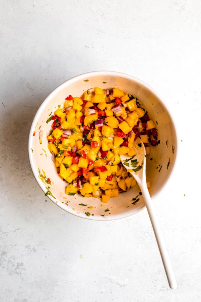 mango salsa in a mixing bowl with a wooden spoon after stirring together.