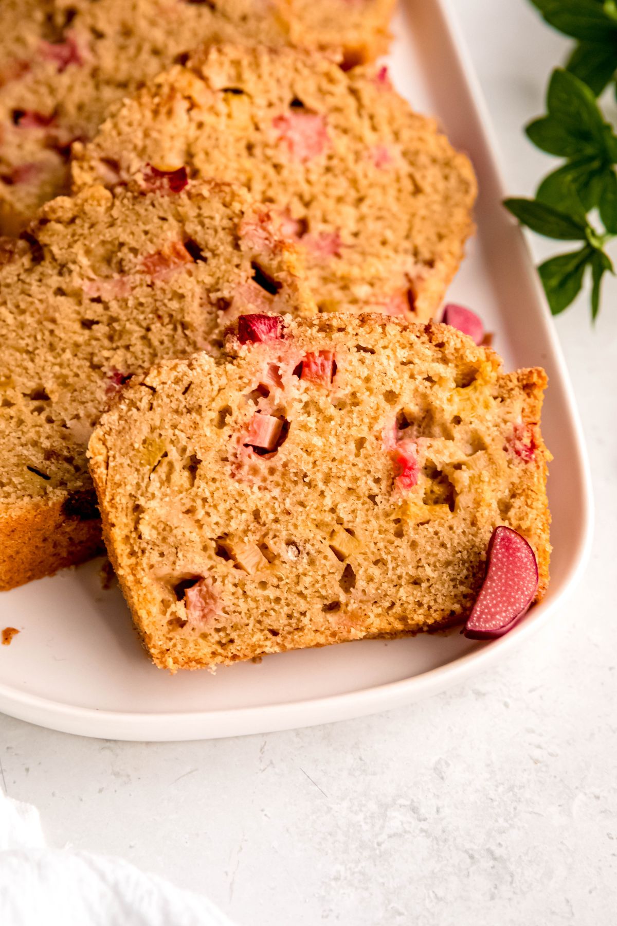 closeup shot of a slice of homemade whole wheat rhubarb quick bread showing the fluffy interior, crackly top, and juicy pops of rhubarb.