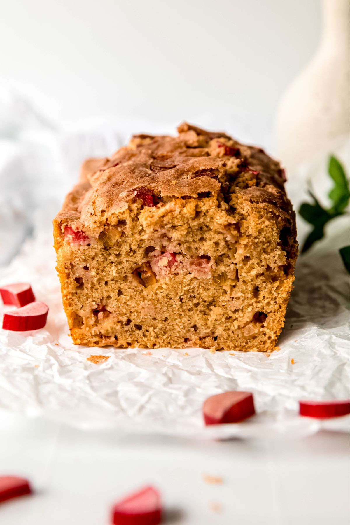 side on view of cinnamon sugar rhubarb bread loaf with a slice taken off, exposing the fluffy internal crumb.