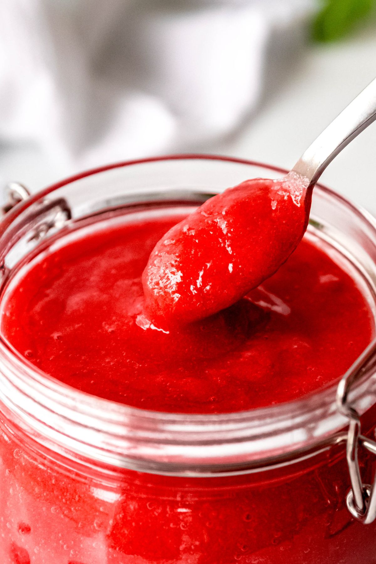 closeup shot of a silver spoon taking a spoonful of homemade rhubarb sauce from the clear mason jar showing its thick, smooth consistency.