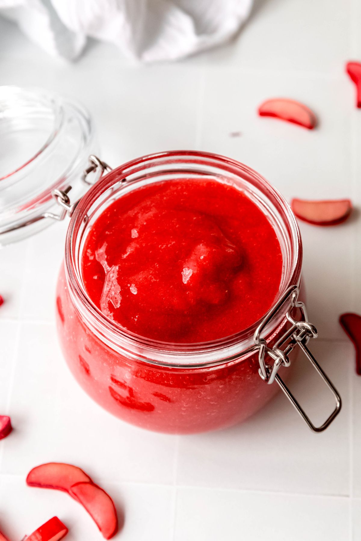 45 degree overhead shot of vibrant pink-red rhubarb sauce in a flip top mason jar on a white tile table.