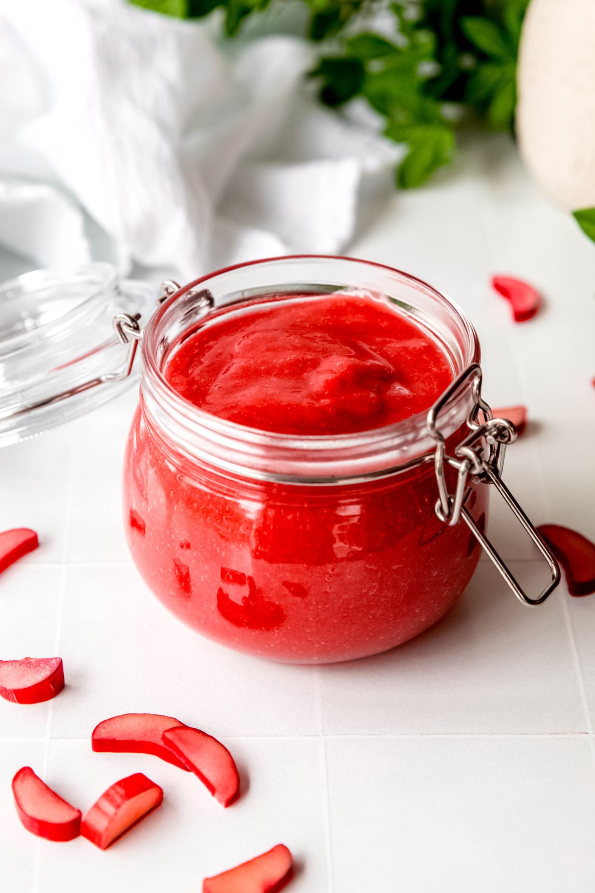 small flip-lid mason jar filled with homemade rhubarb sauce on a white tile table with slices of fresh rhubarb stalks.
