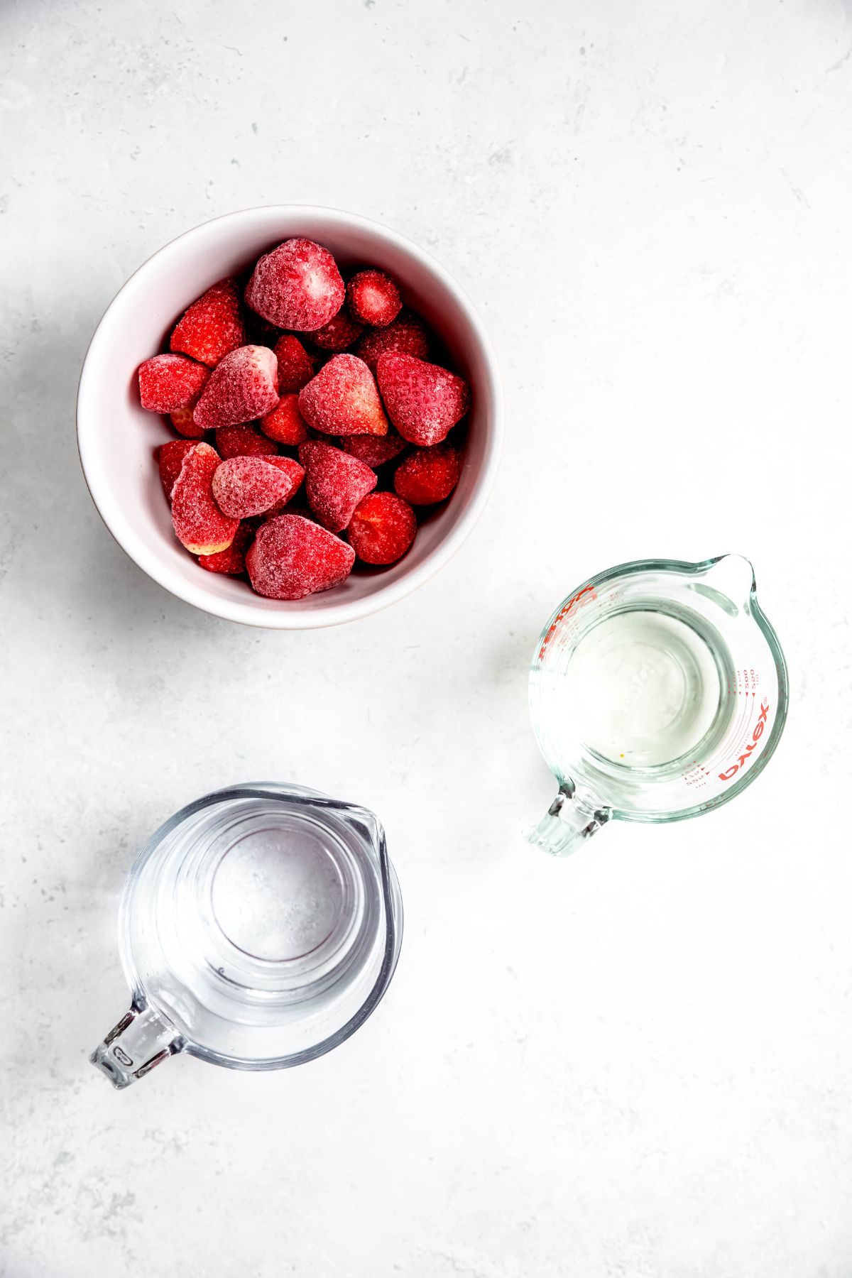Ingredients needed to make homemade strawberry sorbet measured out on a white table.