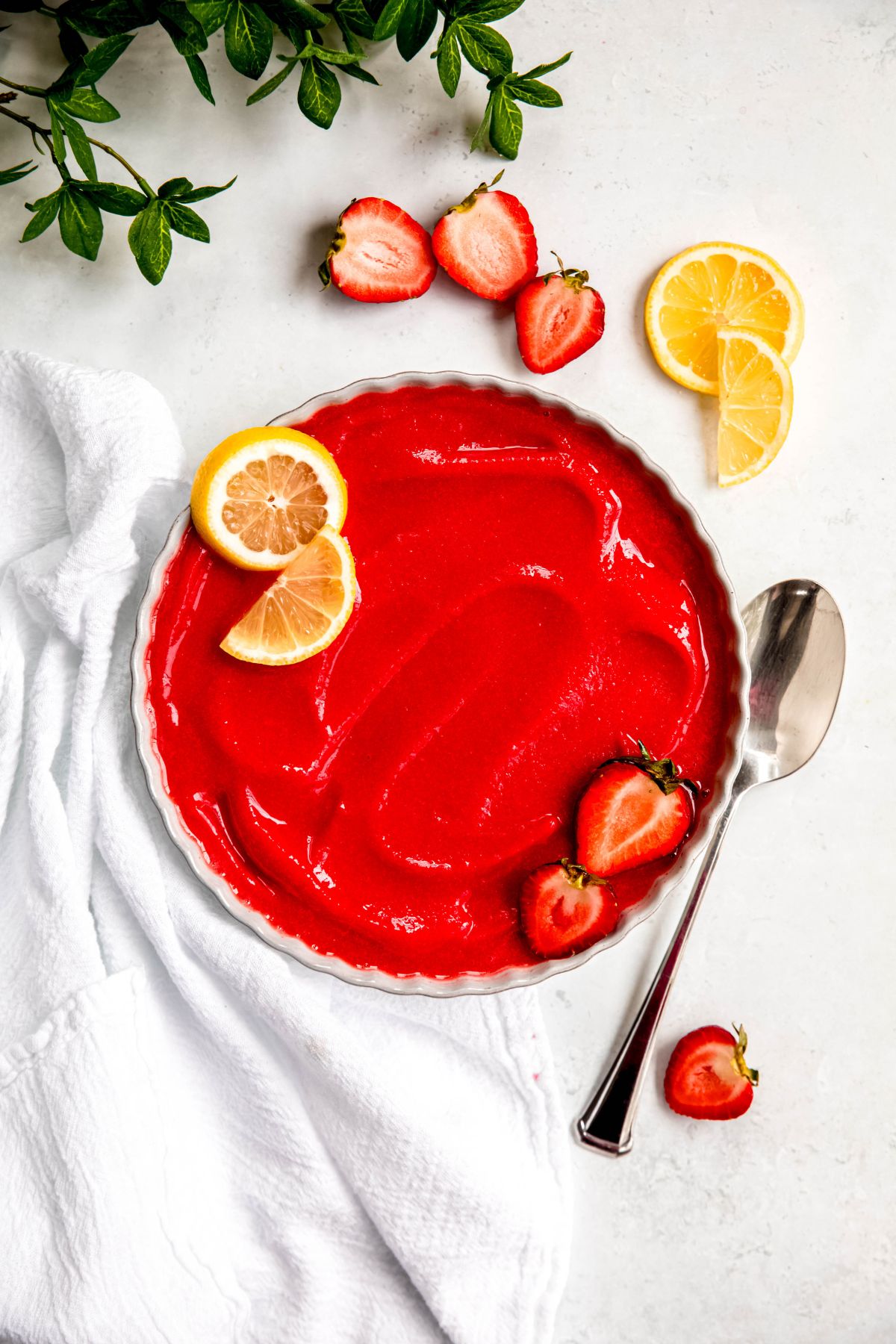 overhead shot of a bowl of strawberry lemon sorbet on a white table with sliced berries and lemon slices and a silver spoon.