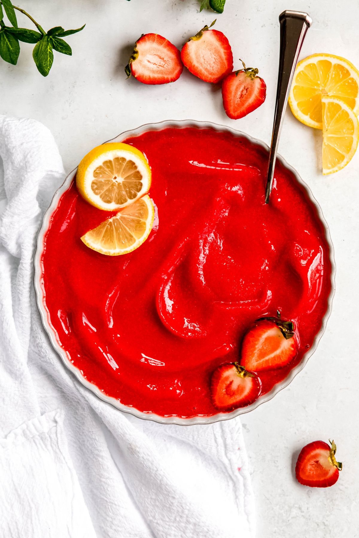 overhead shot of a scalloped white serving bowl filled with blender strawberry sorbet topped with lemon slices and halved strawberries with a silver spoon.
