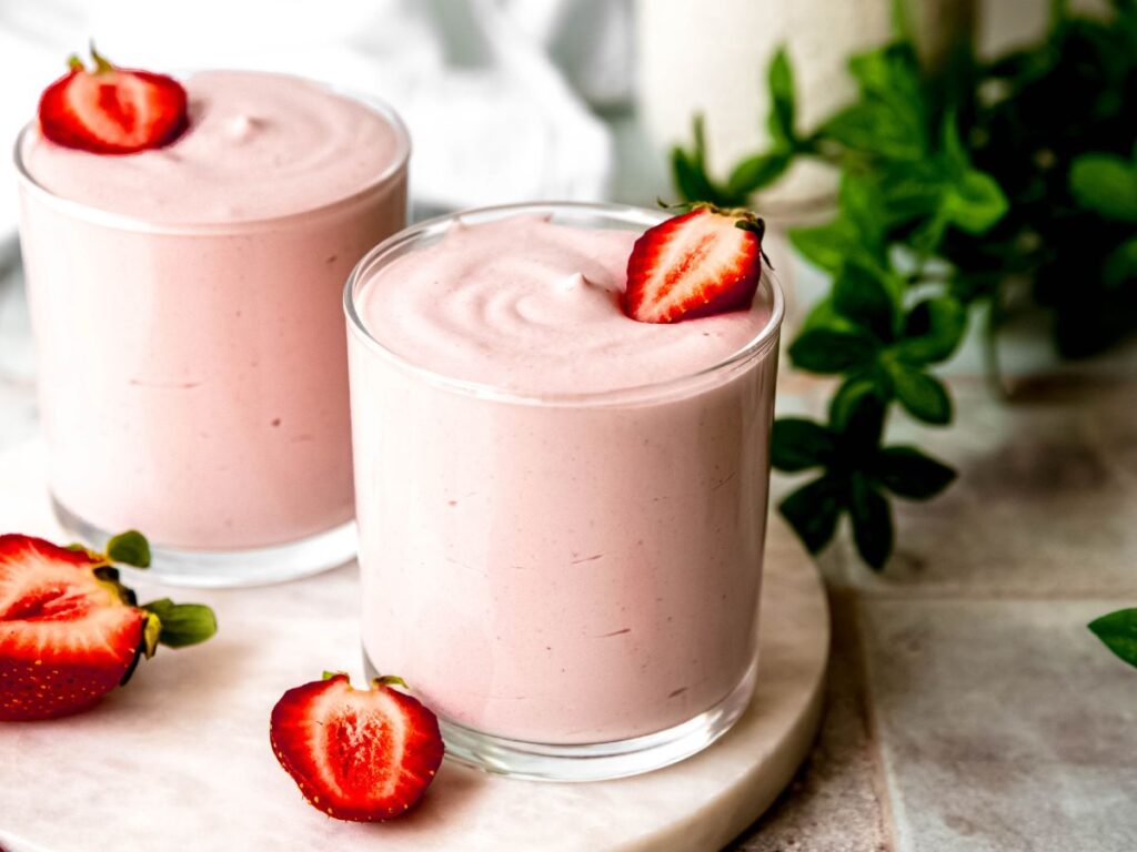 horizontally framed hero shot of high protein strawberry mousse fluff in two rocks glasses topped with halved strawberries.