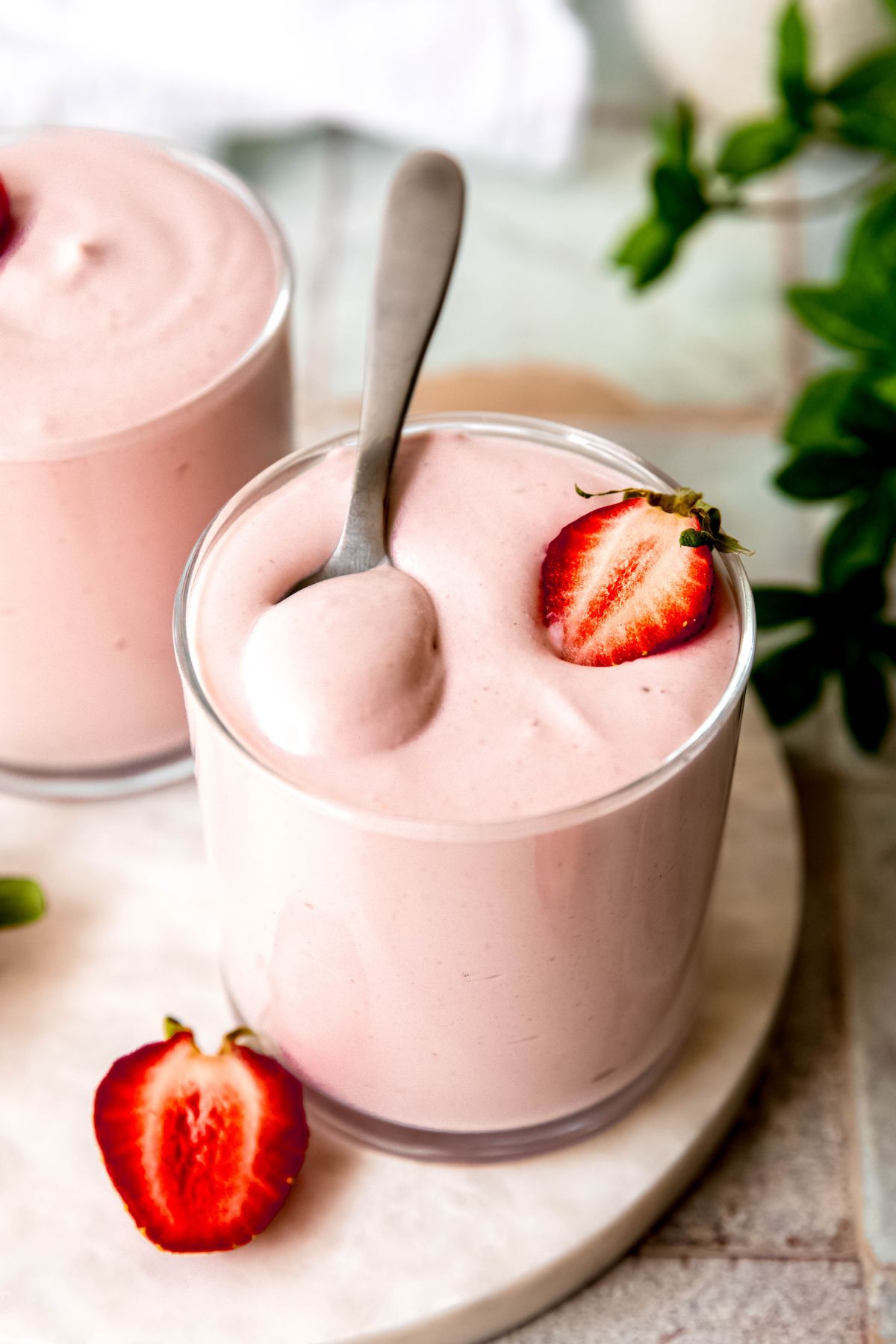 silver spoon in a glass of strawberry protein mousse with a halved strawberry garnish.